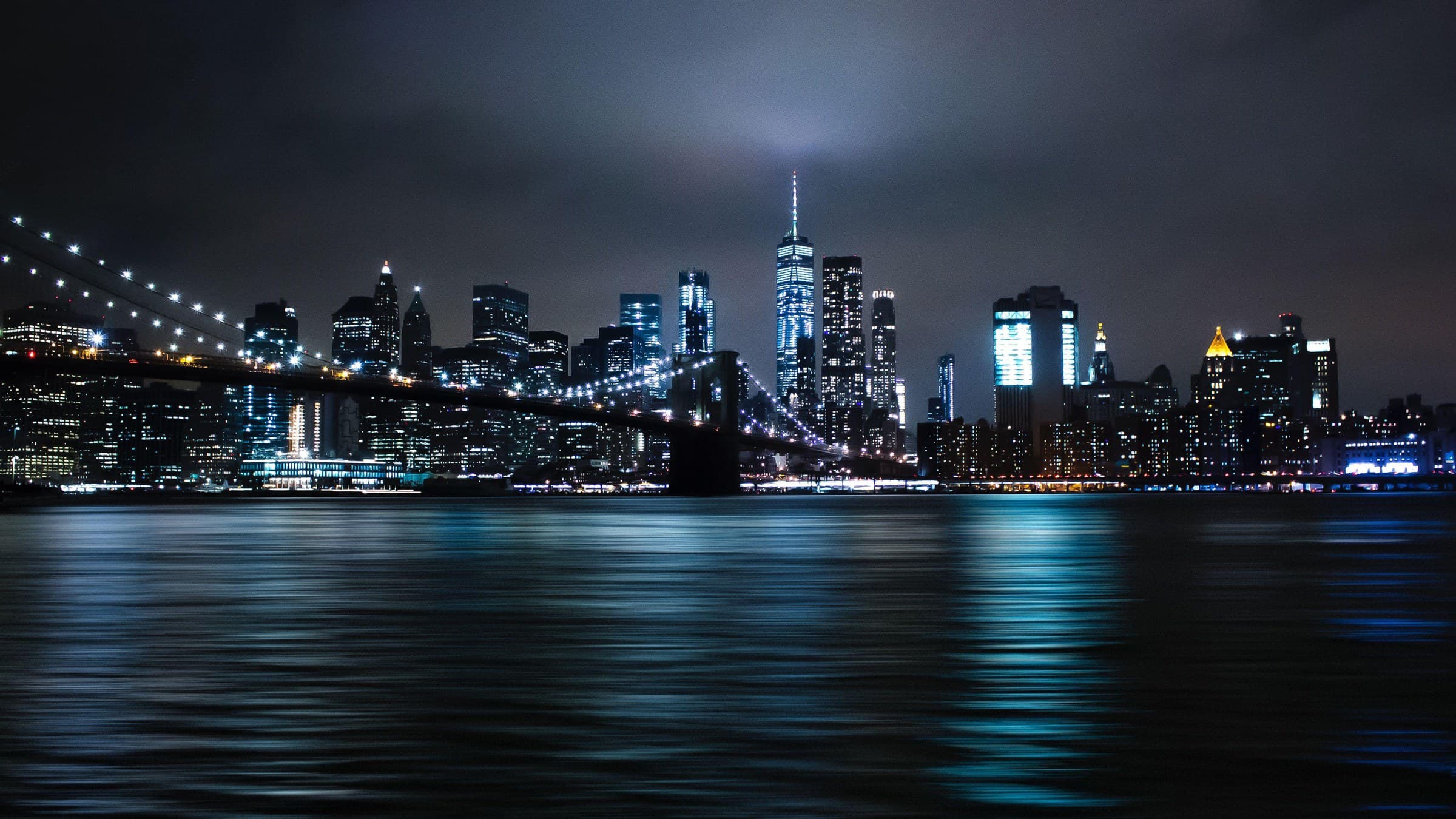 Manhattan at night from the East River, the Brooklyn Bridge lit up.