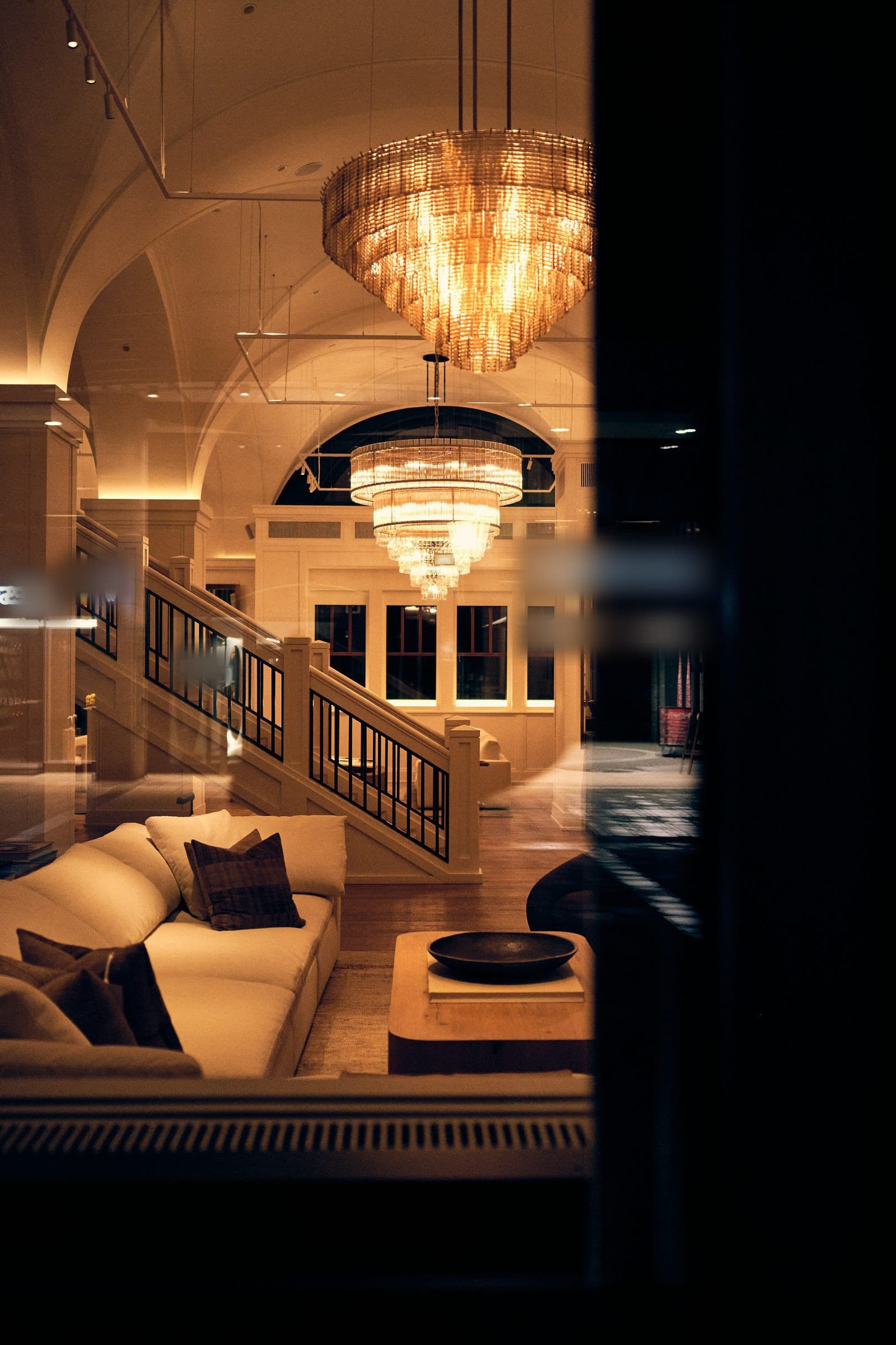 A salon beneath glass chandeliers, low light and pale banquettes.