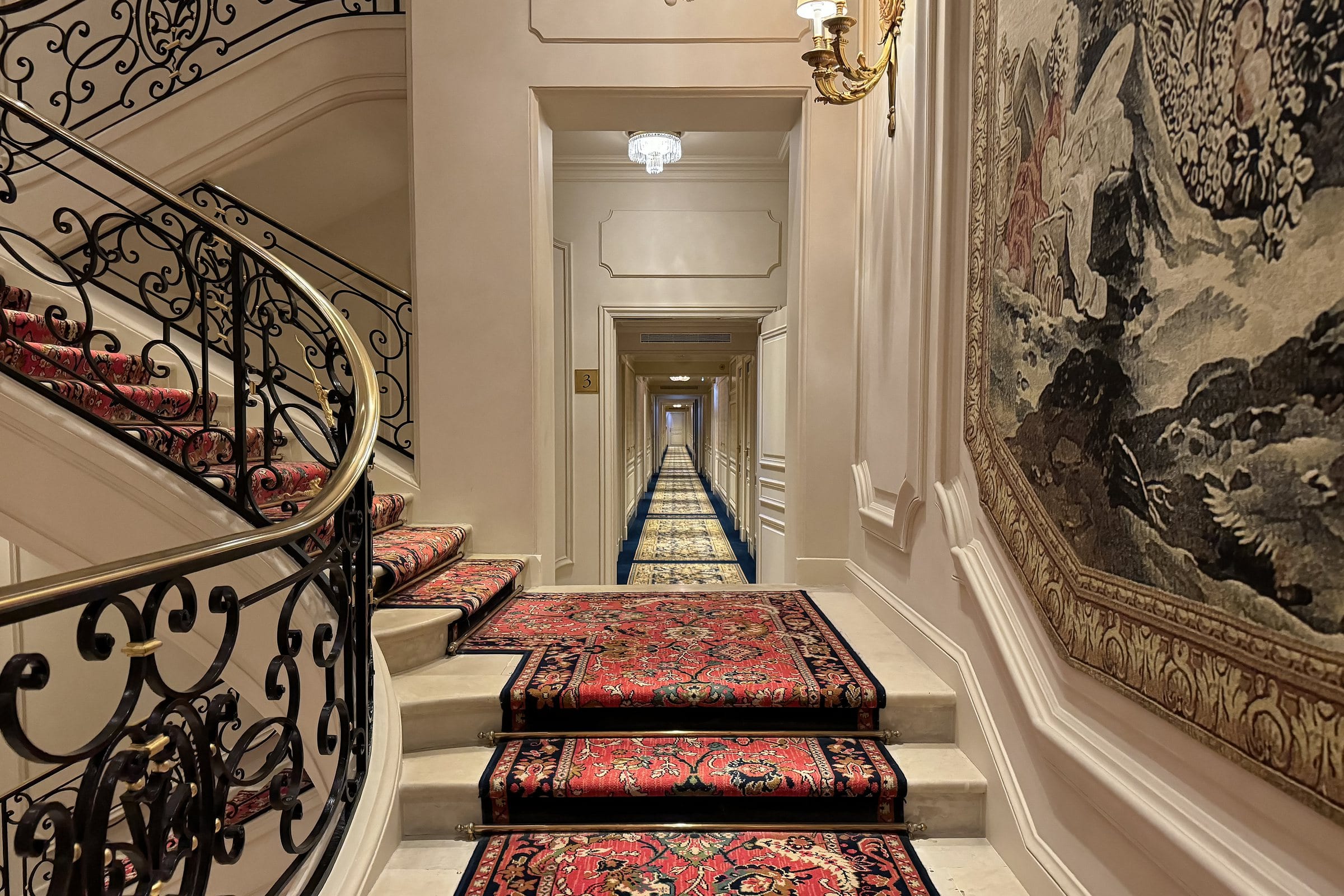 Staircase and corridor of a Paris palace hotel, wrought-iron railing and carpet.