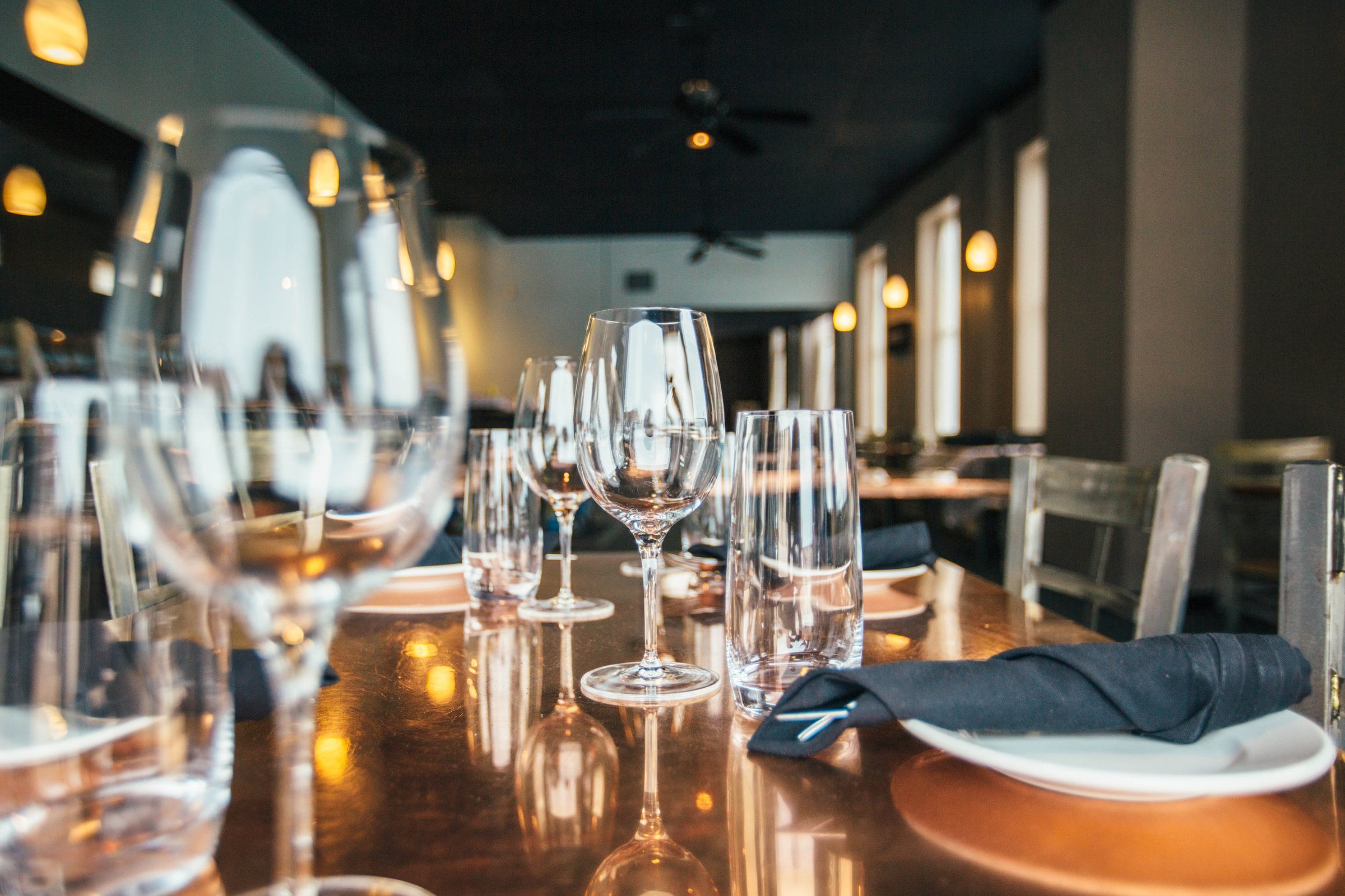 Une table dressée vue à hauteur de nappe, cuivre poli et verres alignés.