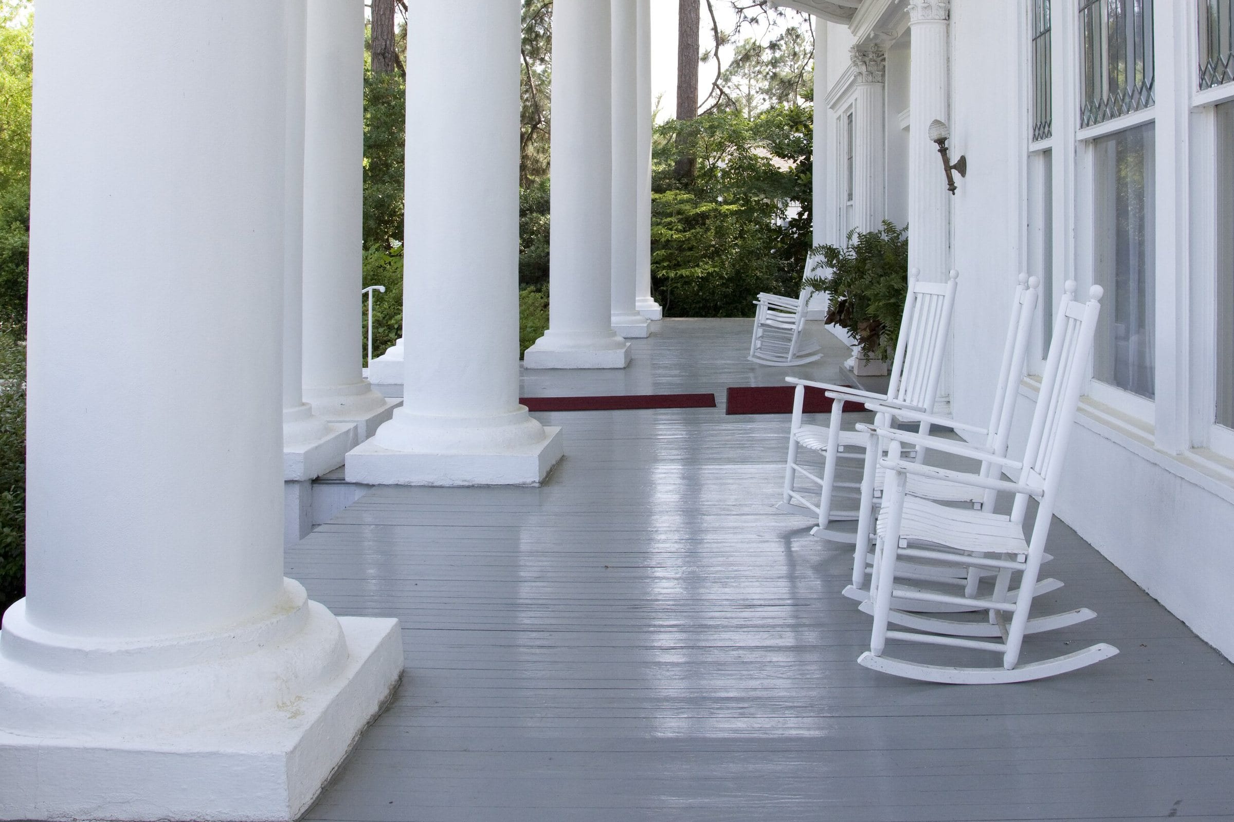 La véranda d'une grande maison blanche du Sud, colonnes et fauteuils.