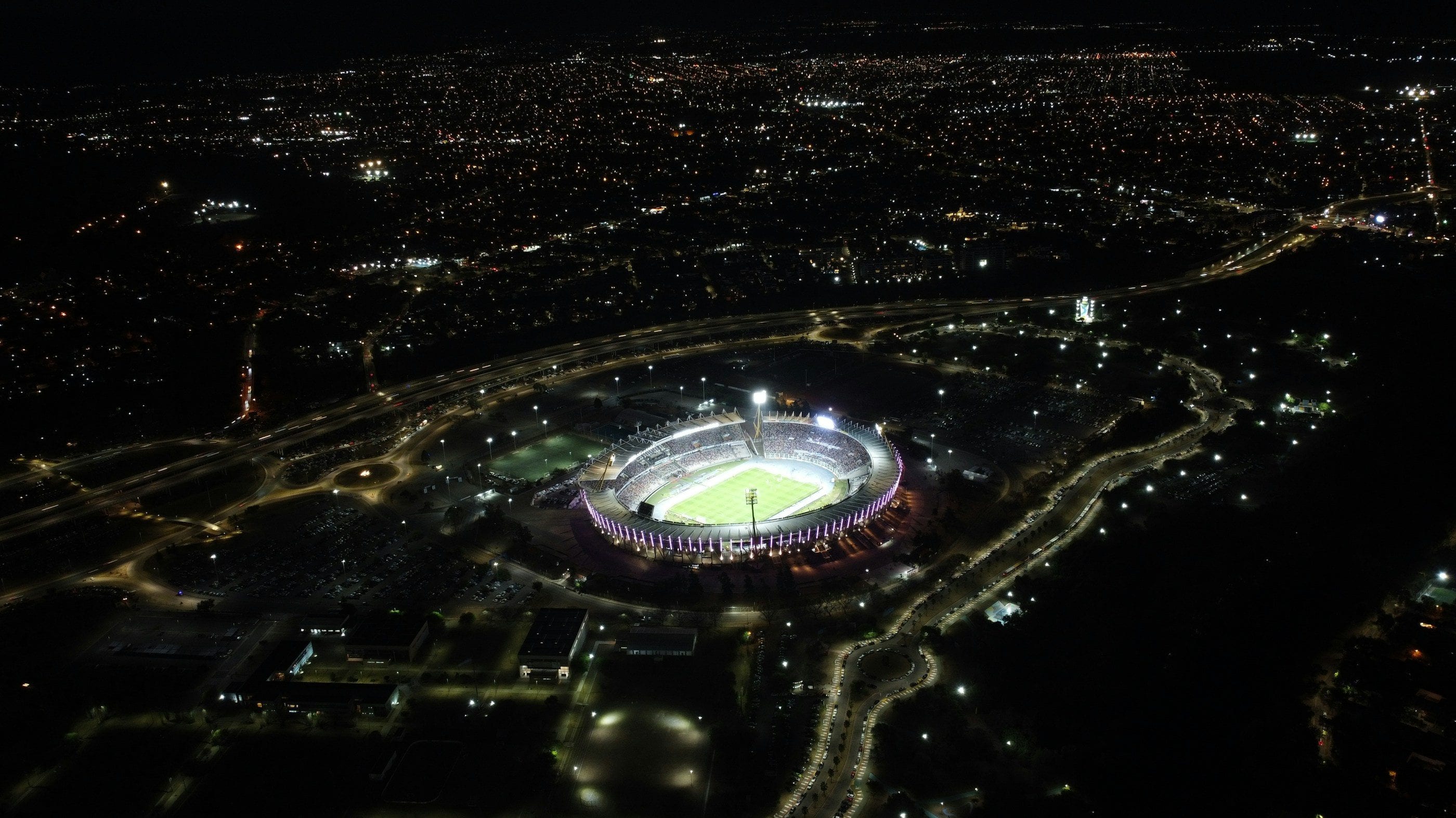 A stadium lit up at the heart of a city at night.