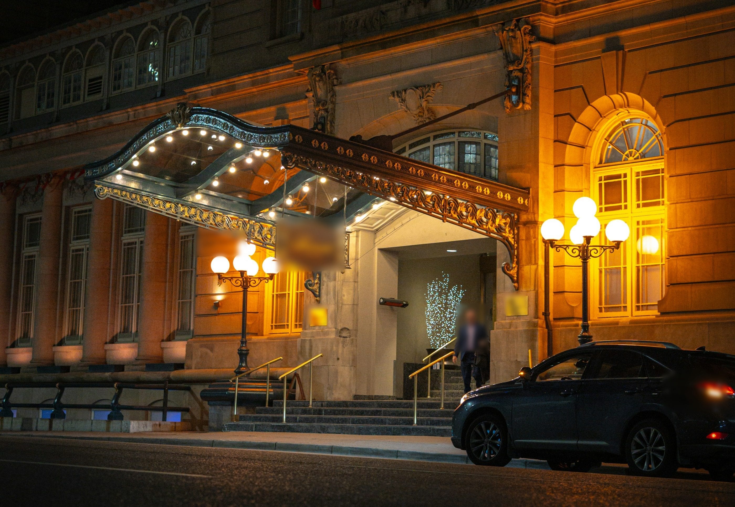 A grand hotel entrance at night, its canopy lit and a car waiting.