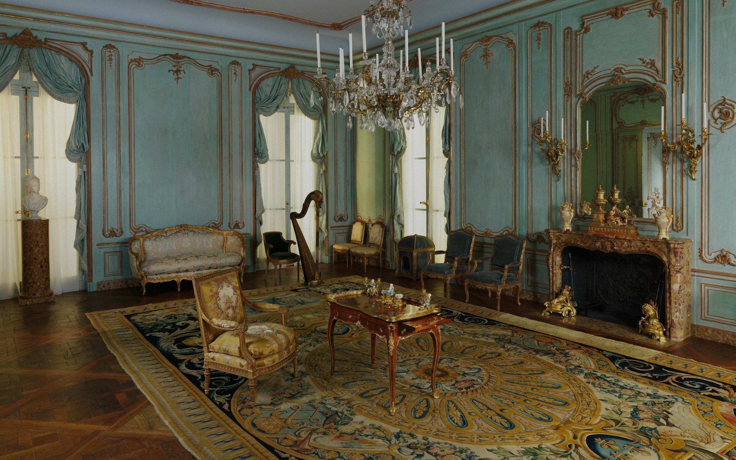 An eighteenth-century salon with pale green and gilt panelling beneath a crystal chandelier.