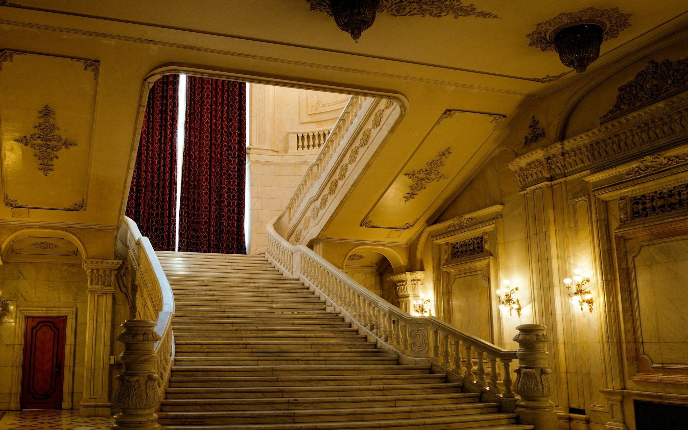 Un grand escalier de marbre dans la pénombre dorée d'un palais.