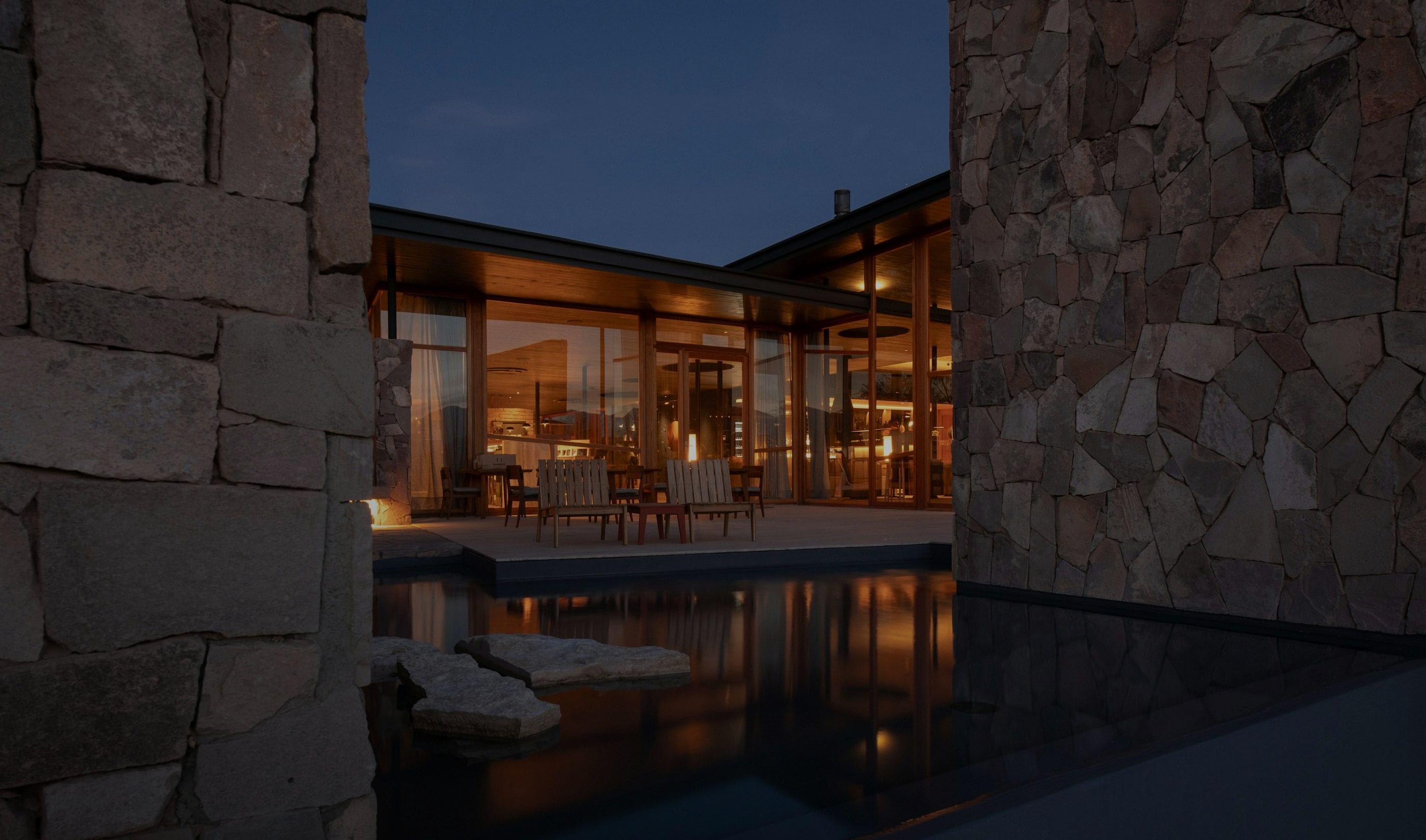 Una villa de piedra y cristal iluminada al atardecer, reflejada en su estanque.