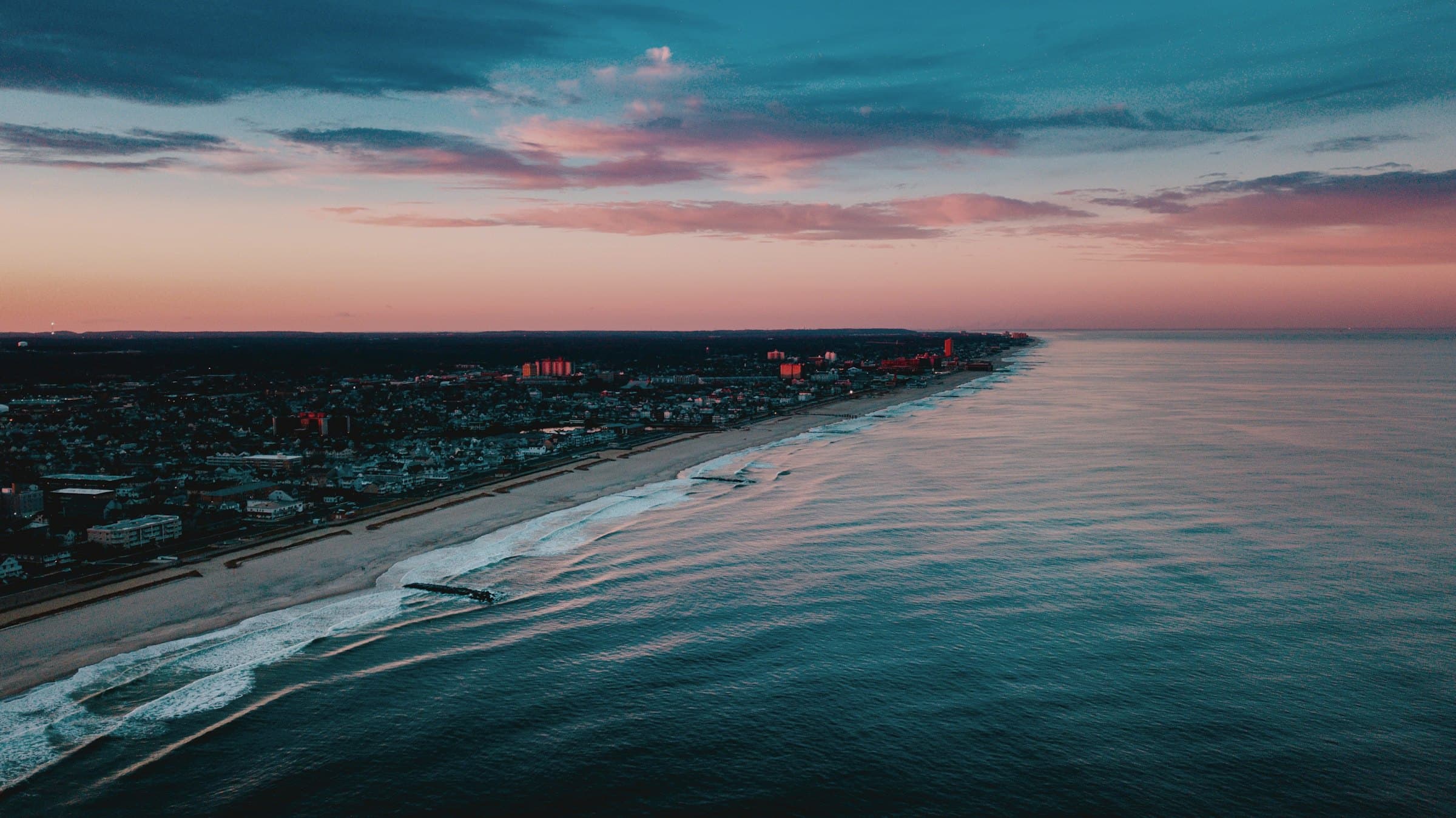 A coastline at dusk, the sea beneath a pink sky.