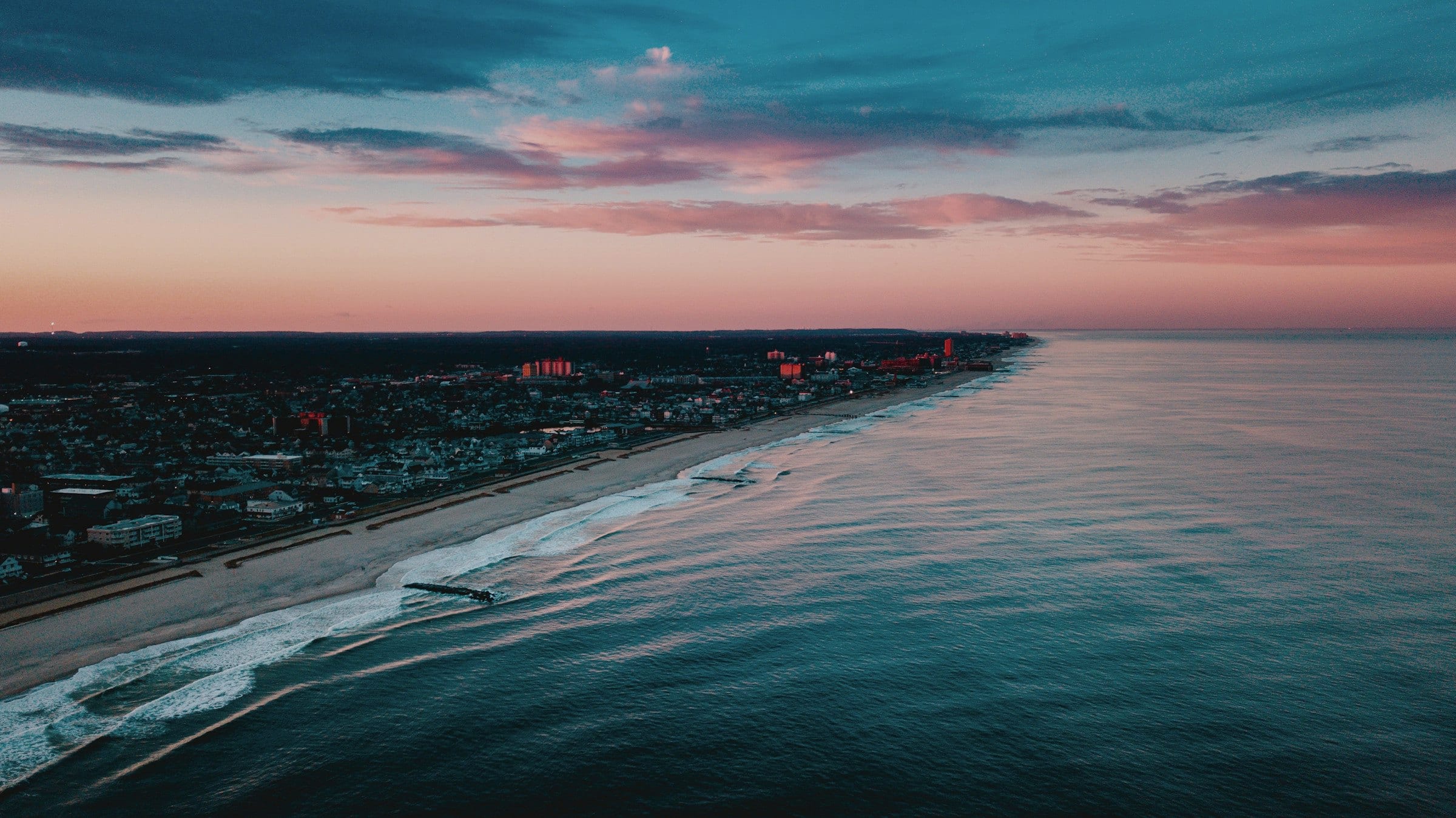 A coastline seen from altitude at dusk: the city, the shore and the open horizon.