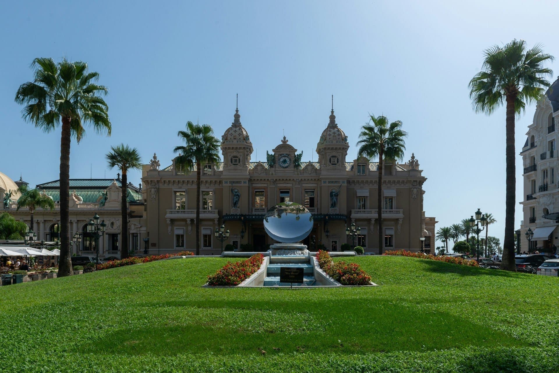 The façade of the Casino de Monte-Carlo on a summer day, palm trees and lawn in the foreground.