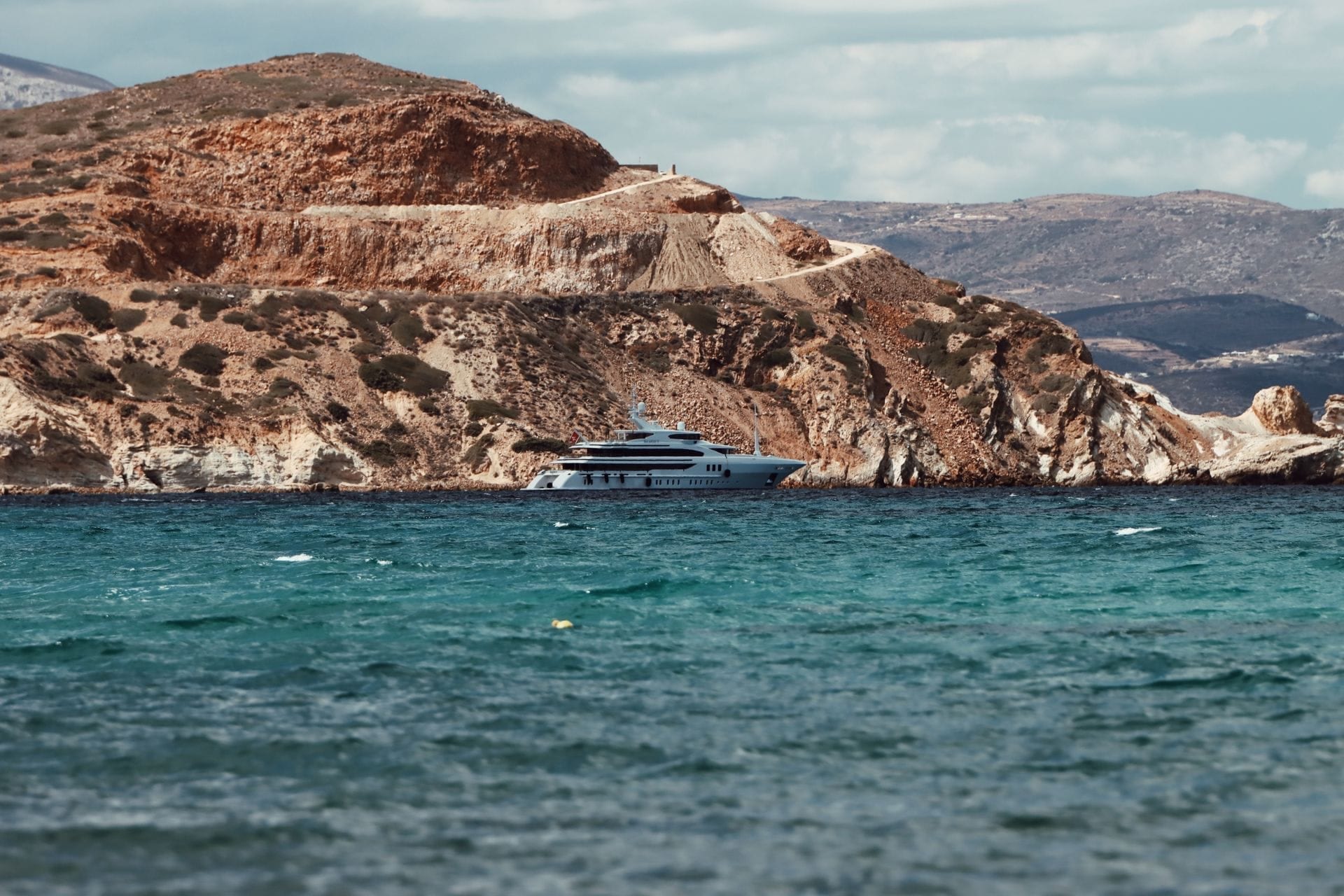 A yacht at anchor below an arid headland, in the Aegean.