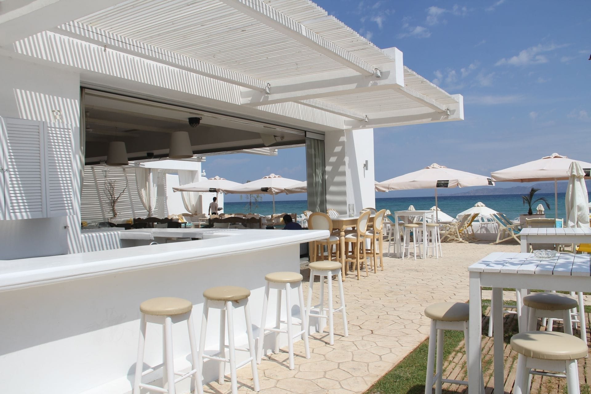 A white beach club, counter and parasols facing the sea.