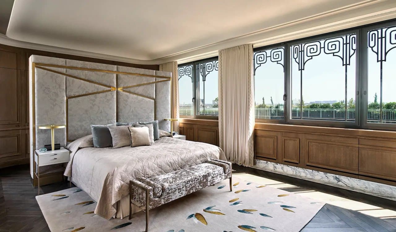 A light-filled suite with tall windows, the bed made, late-afternoon light.