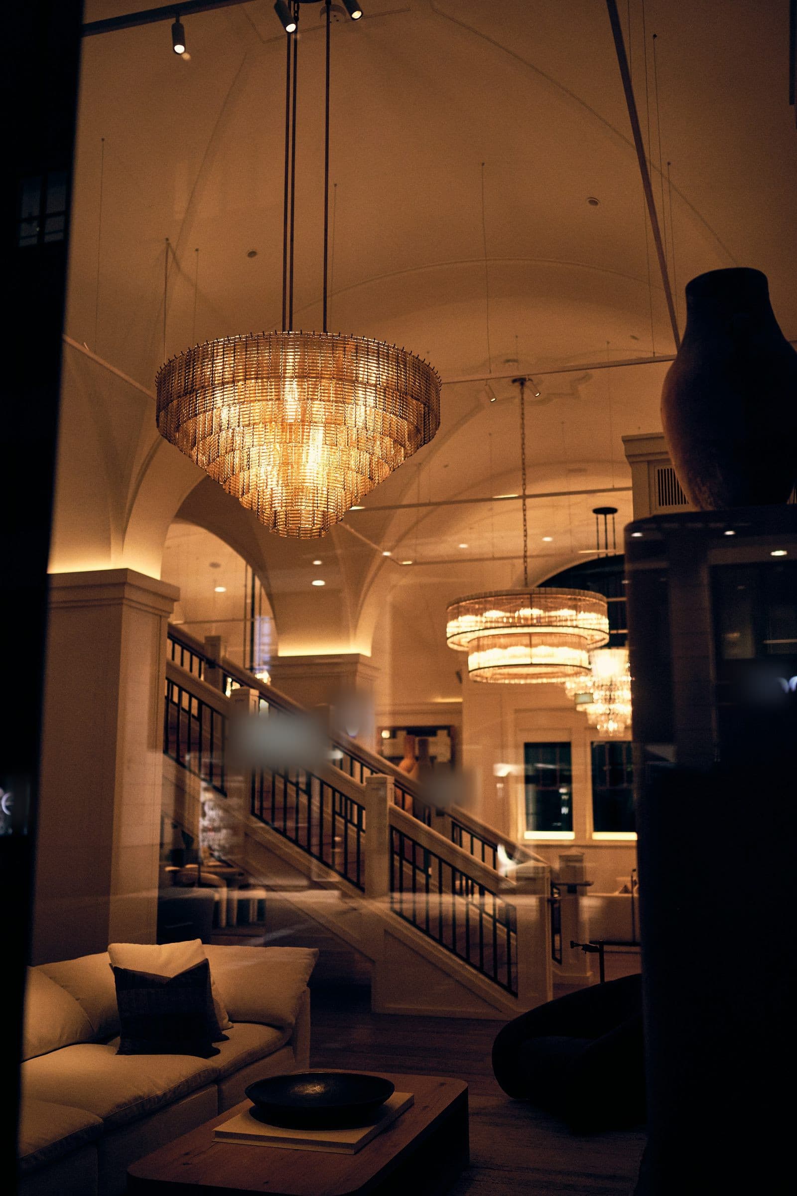 The lobby of a grand hotel at night, chandeliers lit above a staircase.
