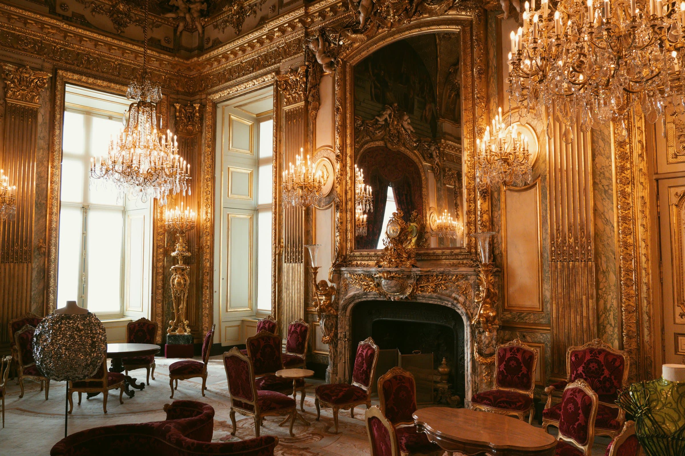 A gilded salon beneath crystal chandeliers, red velvet armchairs.