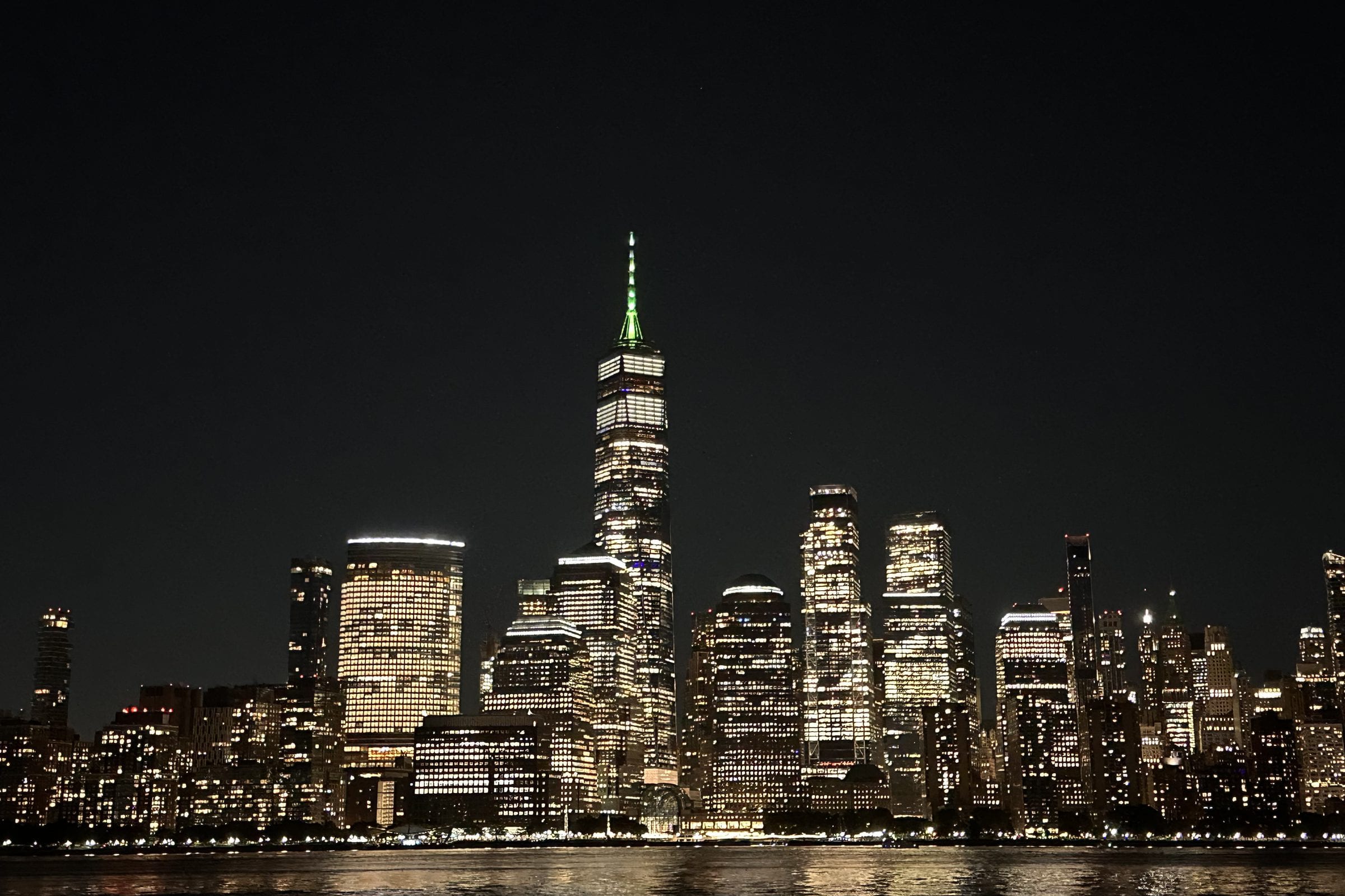 The Lower Manhattan towers at night, seen from the riverbank.